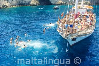 Uczniowie szkoły językowej skaczą do wody z łodzi w Crystal Bay, Comino.